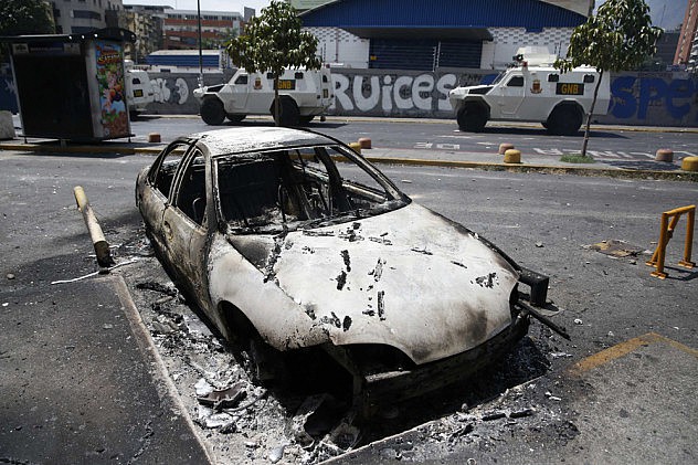 National guard armored vehicles drives past a burnt vehicle after riots in Caracas