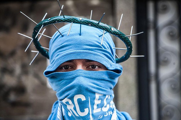 Opositor se hace una "corona de espinas" con clavos y una manguera, con lo que también se hacen "miguelitos" (artefactos para reventar neumáticos). Foto: Boris Vergara, Xinhua